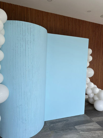 Light blue curved panels with white balloons against a wooden wall.